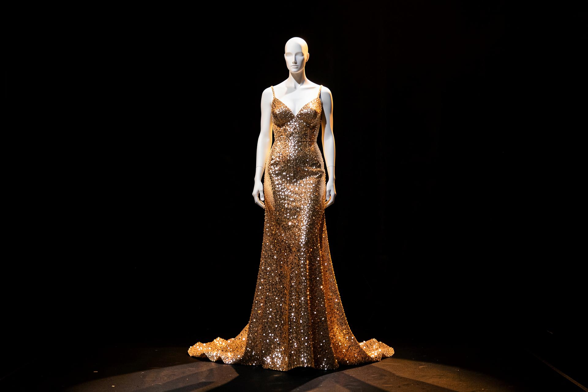 Vestido de festa dourado em manequim sob luz dramática